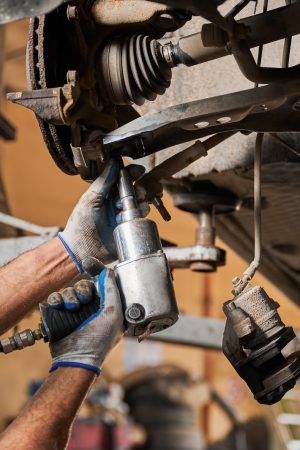Mechanic, engineer servicing car in garage, auto center. Close up mechanic, engineer servicing car in garage, auto center. Hardworking, strong man holding equipment by hands, drilling, looking. Concept of repairing, fixing car.